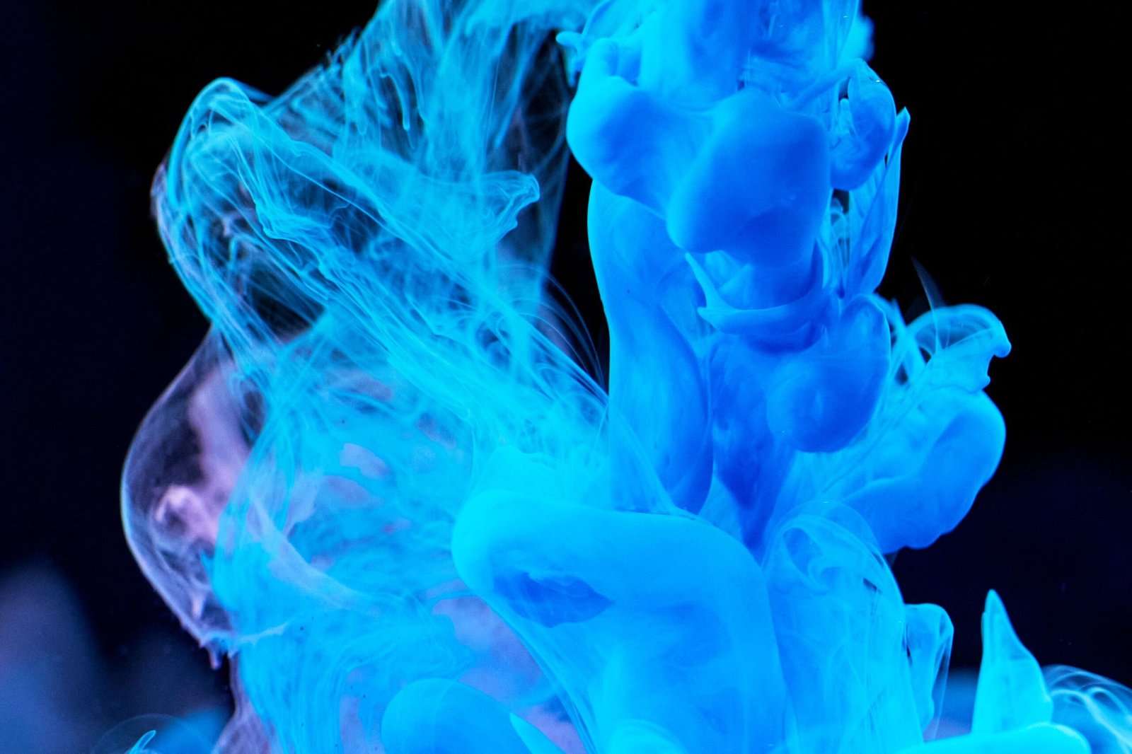 Dynamic blue ink swirls in water creating abstract shapes on a dark backdrop.